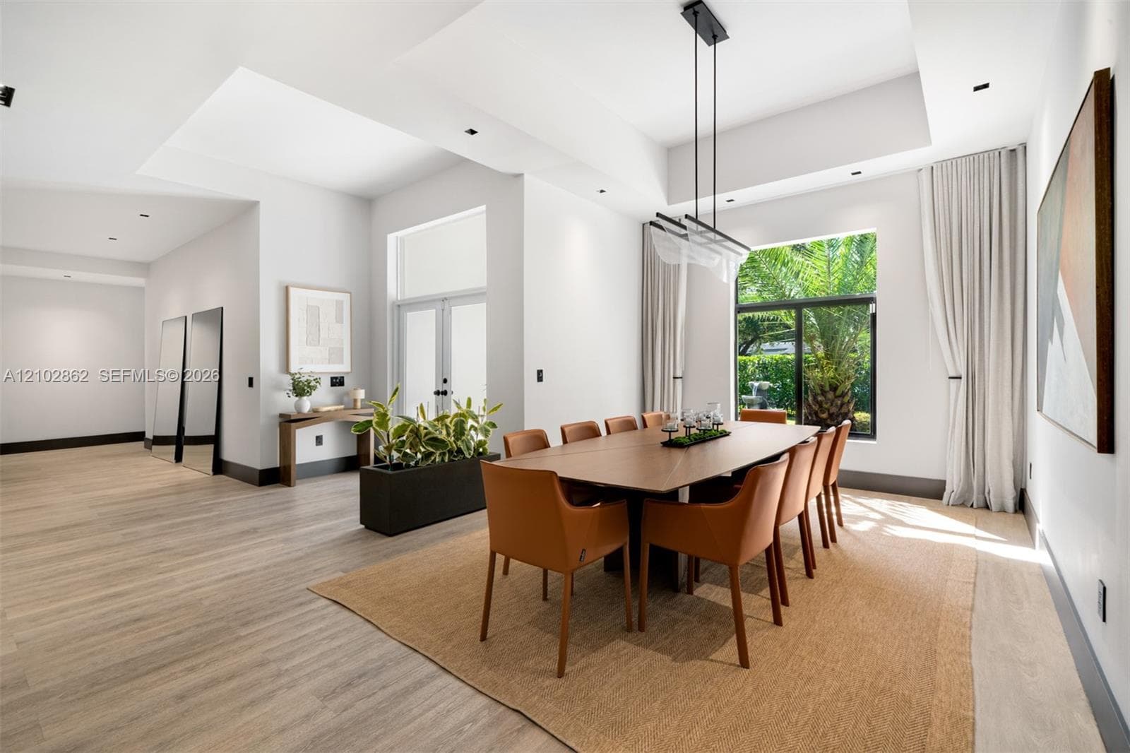Tray ceilings with recessed lighting, wood-finish flooring, large-format windows, modern linear chandelier, and double-door entry