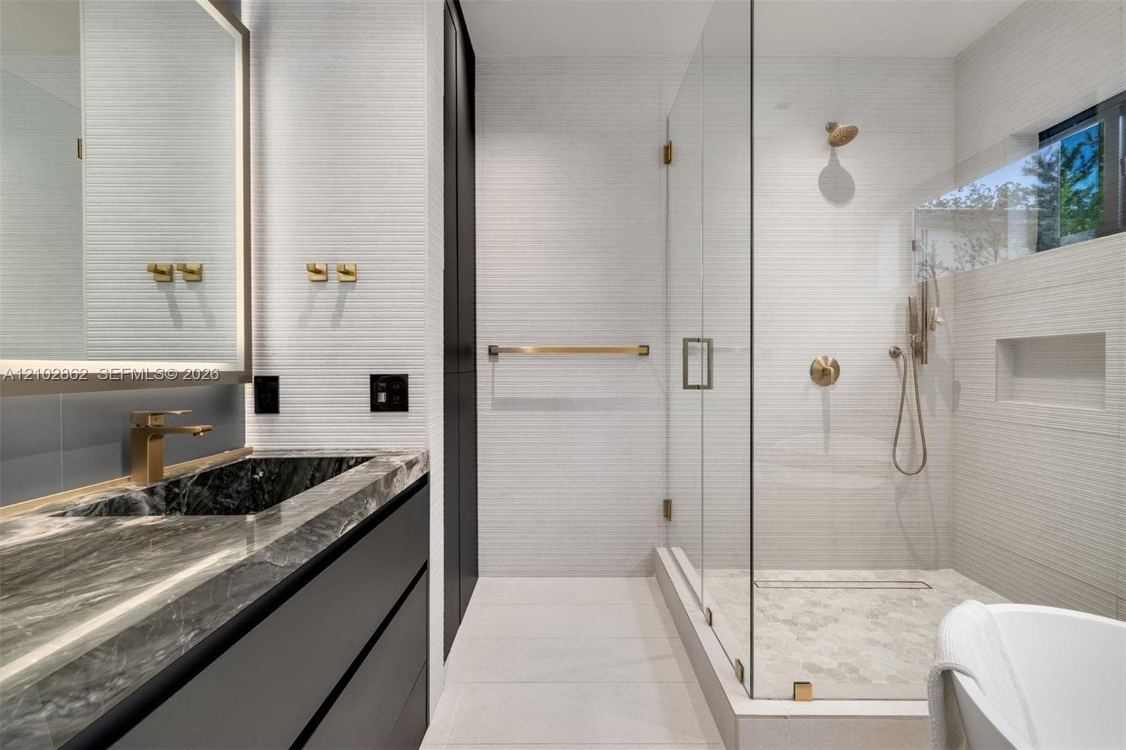 Modern bathroom featuring a floating vanity with stone-finish countertop, walk-in glass-enclosed shower with wall-mounted niche, textured tile walls, and gold-toned plumbing fixtures