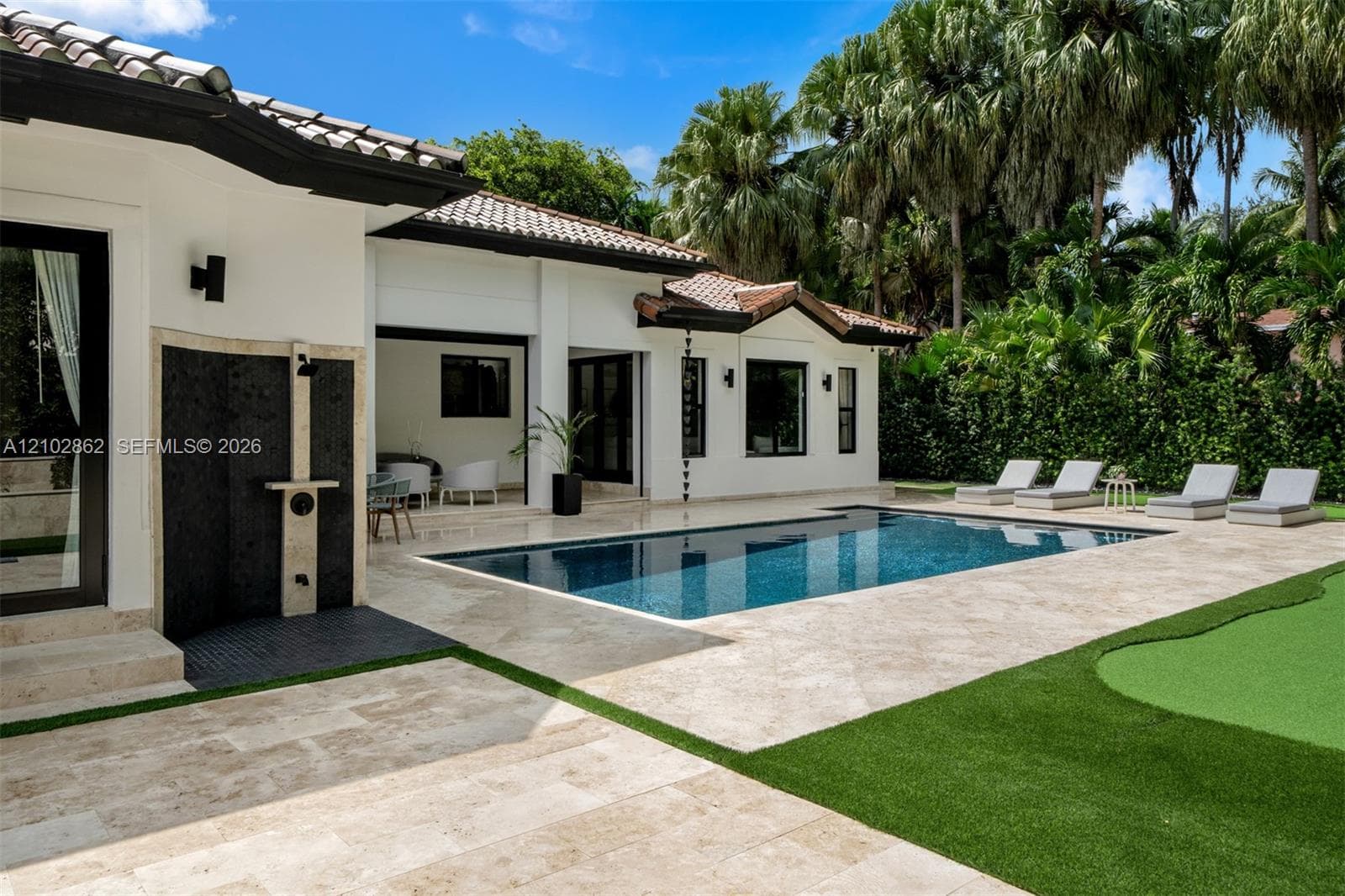 Exterior space featuring a swimming pool, stone paver decking, an outdoor shower with tile backsplash, and a synthetic turf putting green