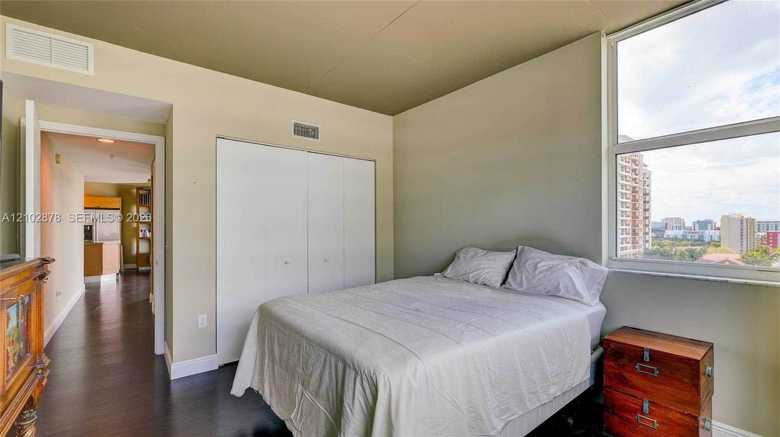 Bedroom featuring wood-finish flooring, a double-door closet, and large windows with exterior urban scenery