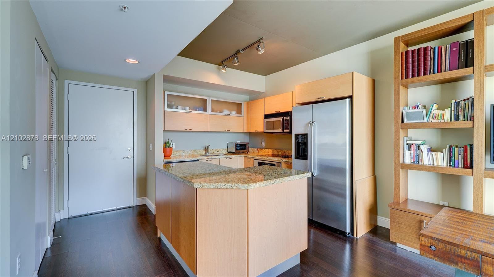 Kitchen featuring wood cabinetry, stone countertops, stainless steel appliances, track lighting, and built-in shelving