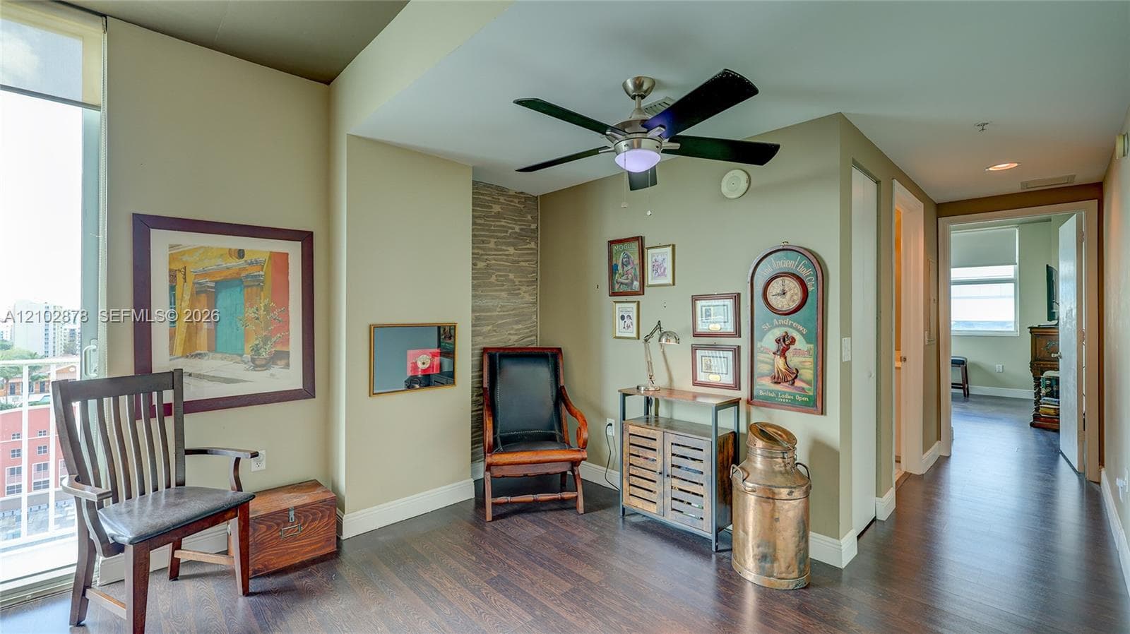 Wood-finish flooring, floor-to-ceiling windows, stacked-stone accent wall, and a multi-blade ceiling fan with integrated lighting