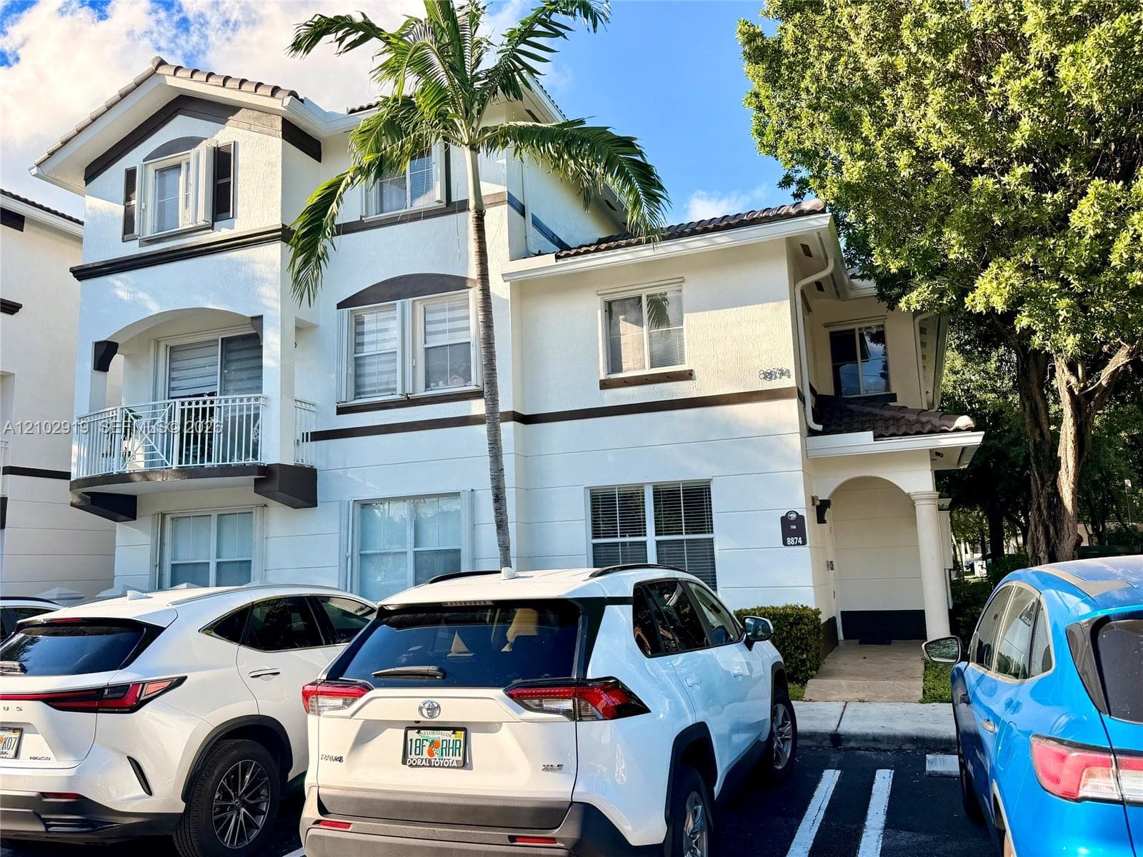 Multi-story stucco exterior featuring a private second-level balcony, decorative trim detailing, tile roofing, and an arched entryway