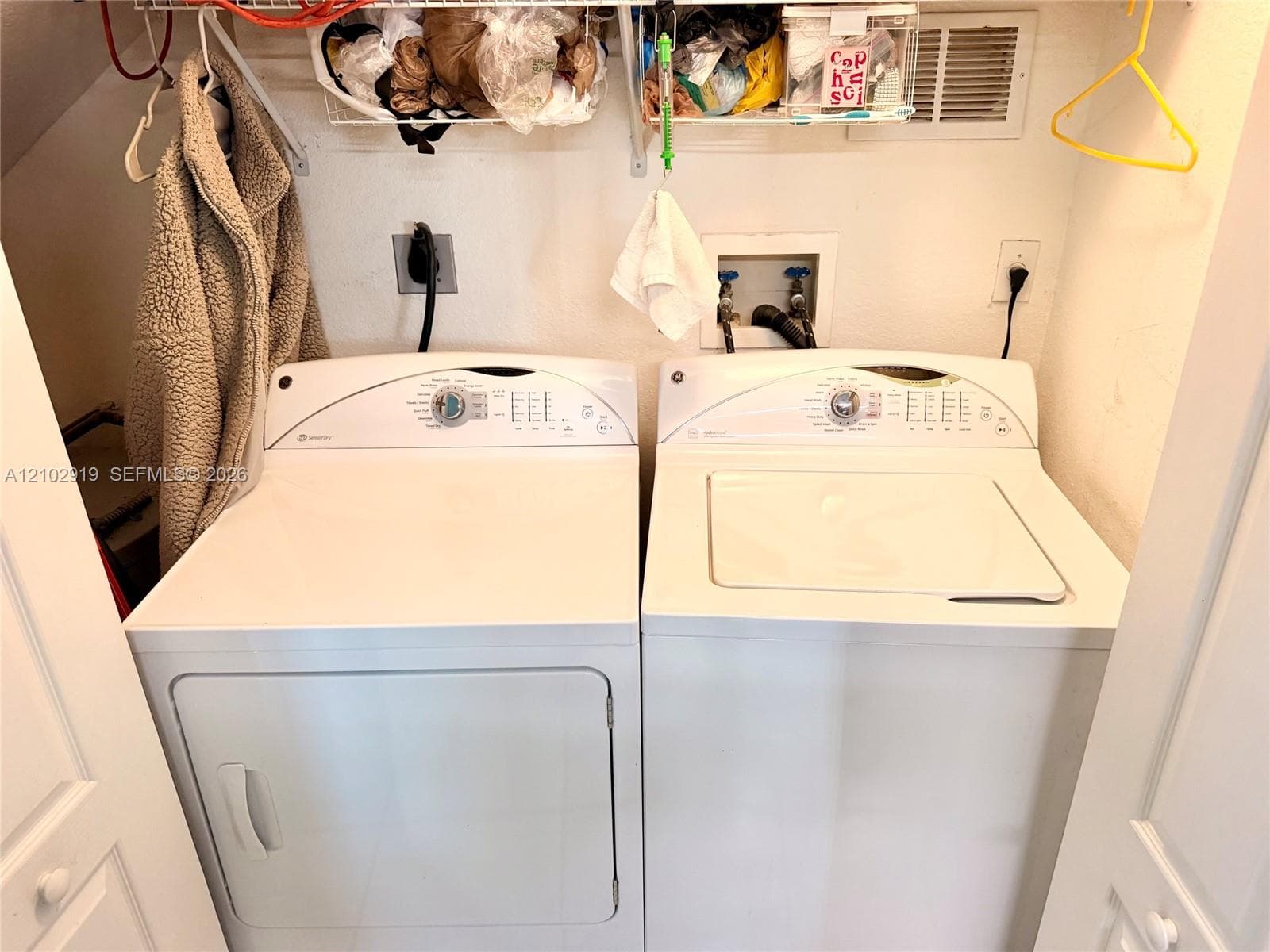 Dedicated laundry area featuring a white top-load washer and white electric dryer, complemented by overhead wire shelving for storage