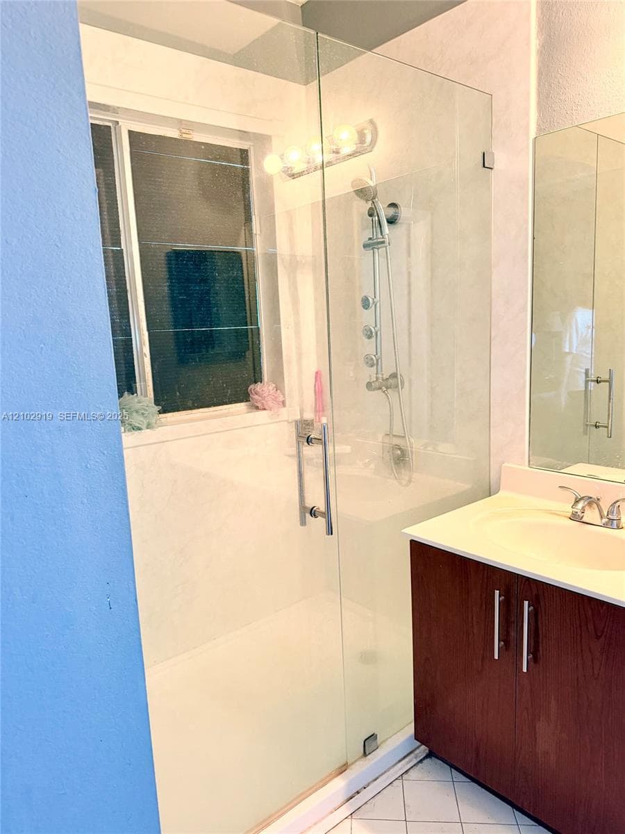 Walk-in shower featuring a glass enclosure, wall-mounted multi-head shower system, and wood-finish vanity with a integrated sink