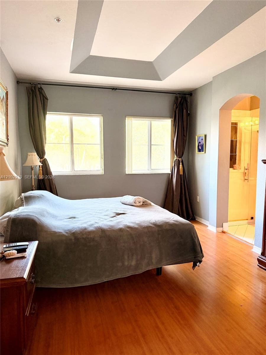 Room featuring a tray ceiling, wood-finish flooring, and an arched doorway