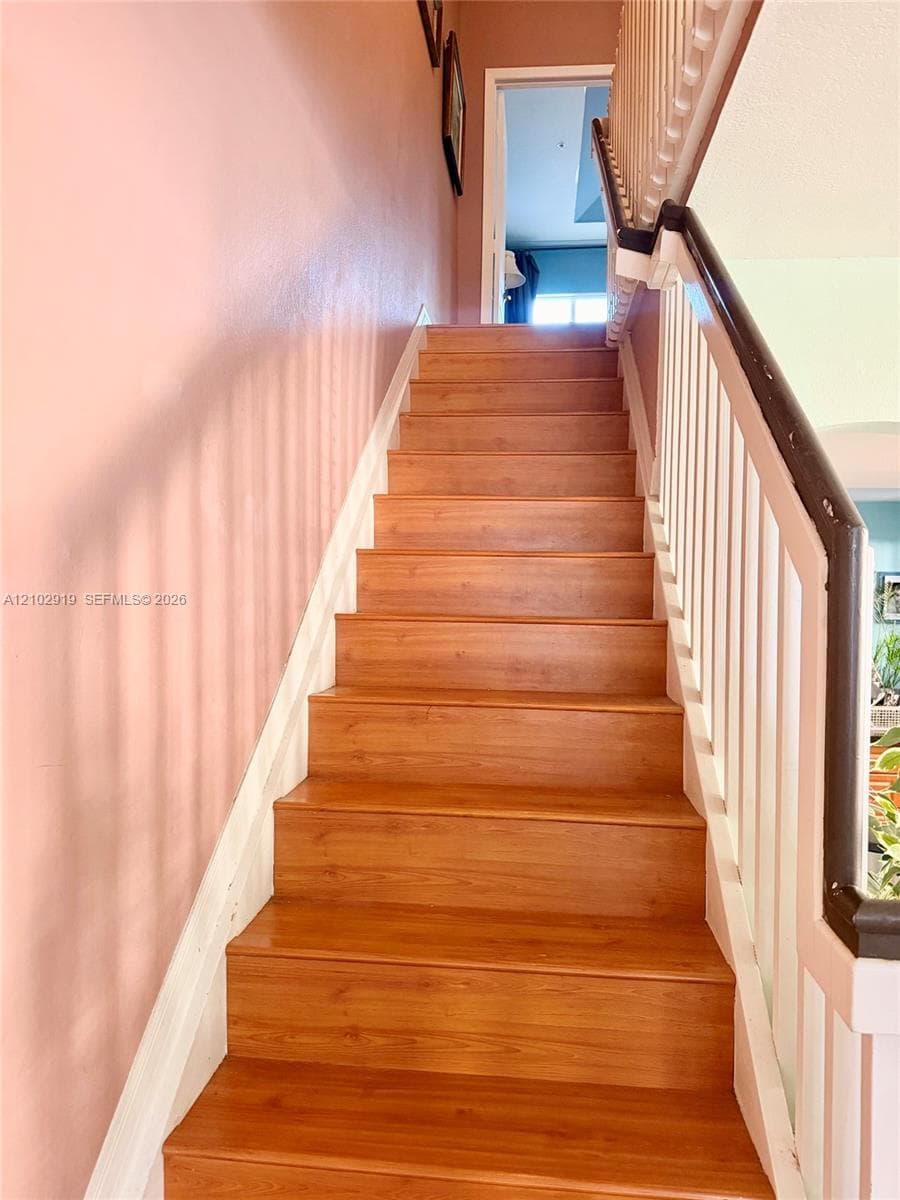 Staircase featuring wood-finish treads, white balusters, and a contrasting dark-toned handrail