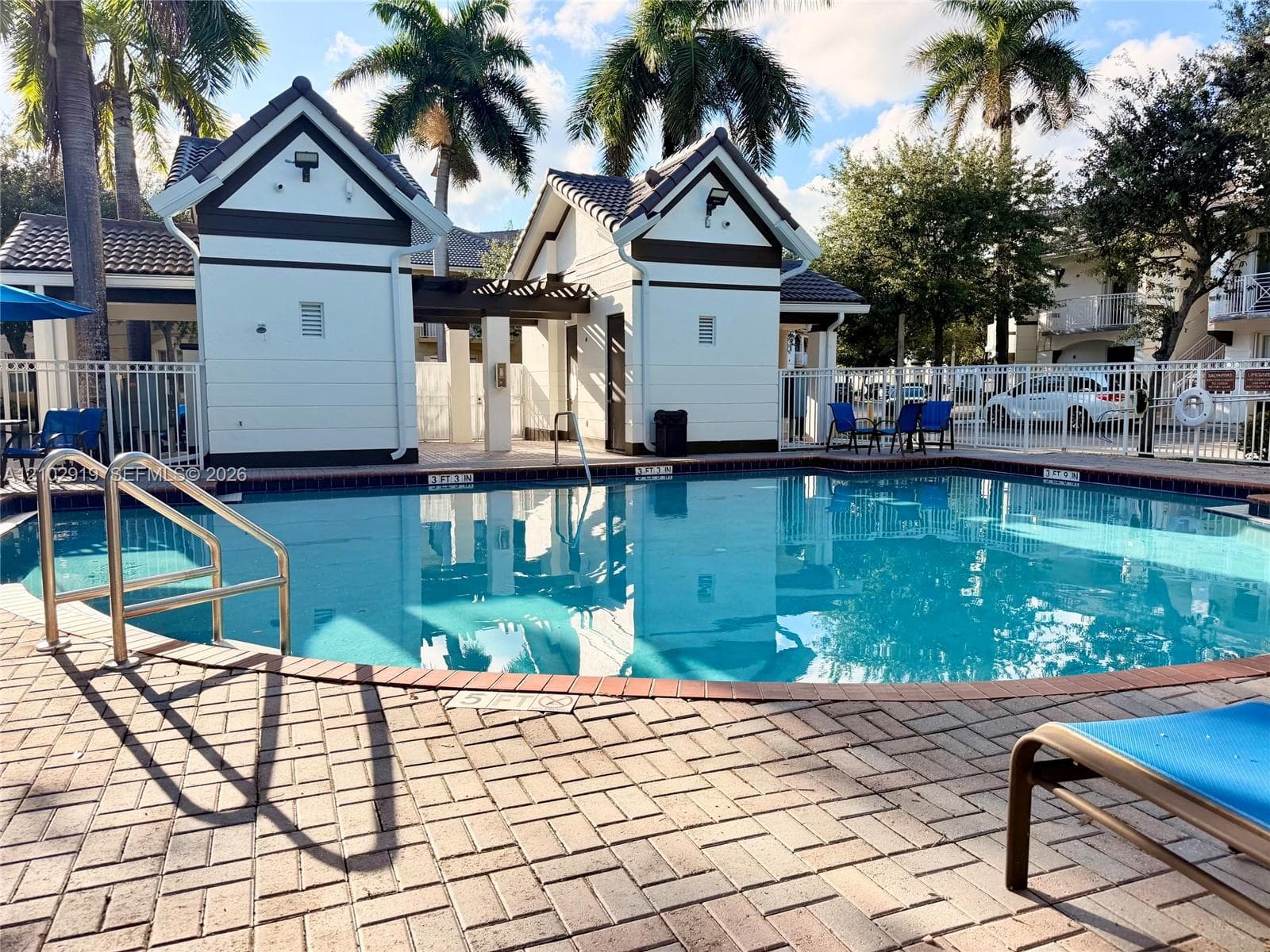 Swimming pool featuring a brick-paver deck, metal pool railing, and two-tone gabled cabanas