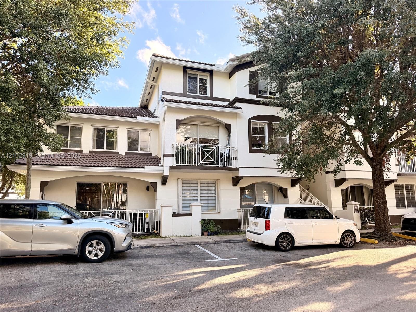 Multi-story stucco exterior featuring a tiled roof, upper-level balcony with decorative railing, and ground-level covered patio