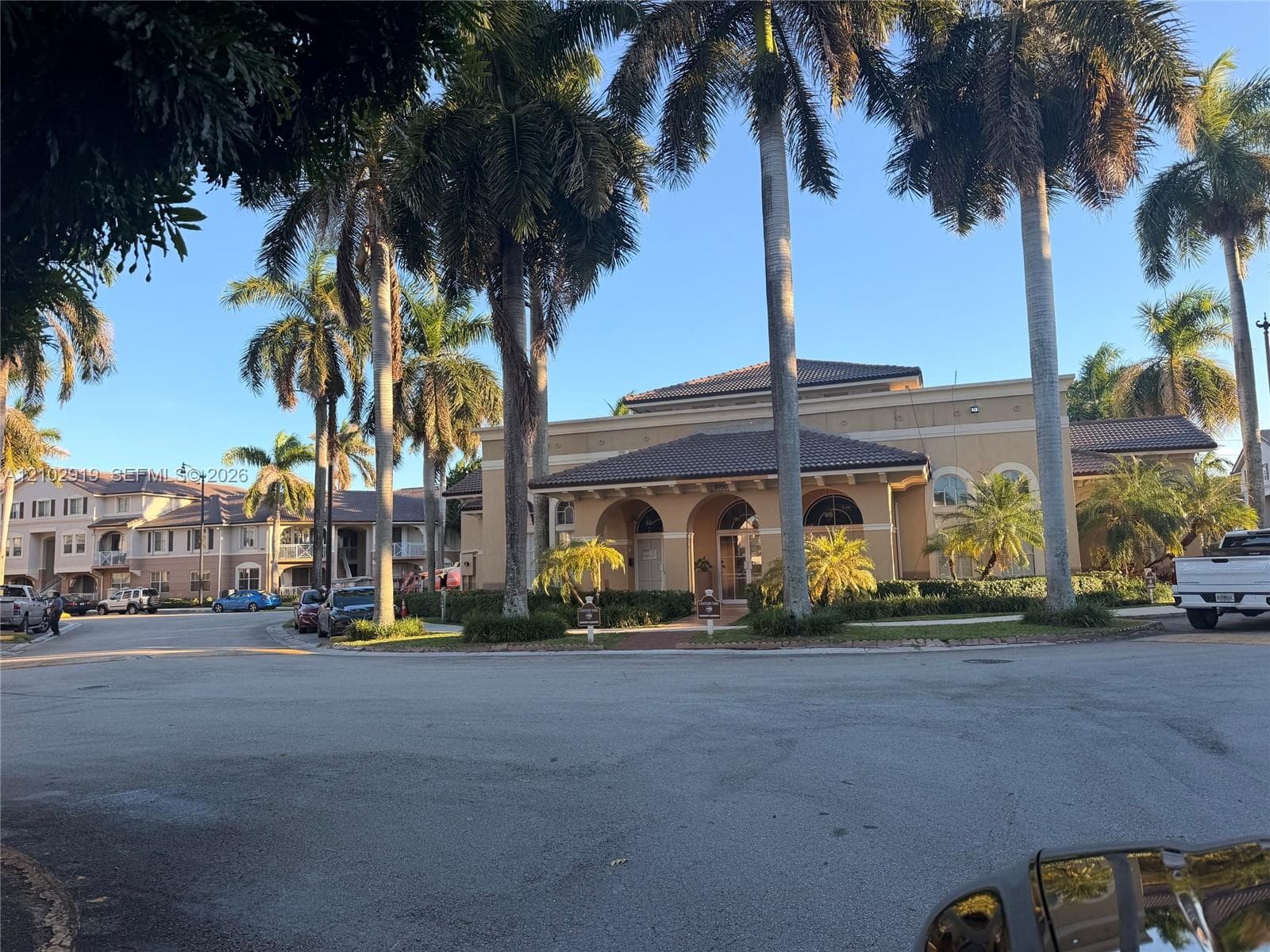 Stucco exterior with a tiled roof, arched covered entryway, and mature palm trees