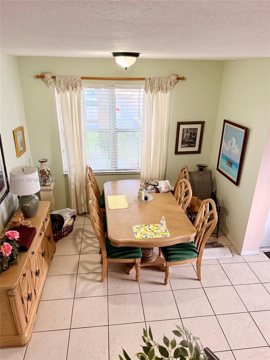 Dining area featuring large-format ceramic tile flooring, a window with horizontal blinds, and a central flush-mount ceiling light fixture