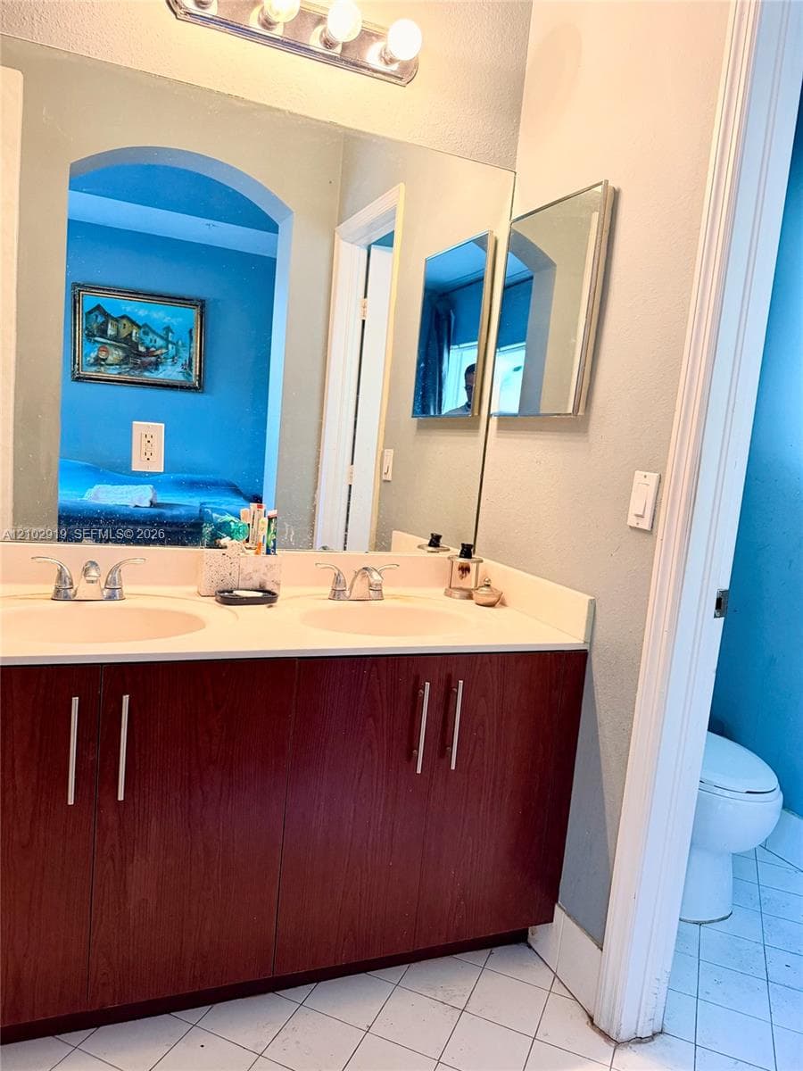 Dual-sink vanity with dark wood-finish cabinetry, light-toned countertop, brushed metal hardware, and full-width vanity mirror with a three-bulb light fixture