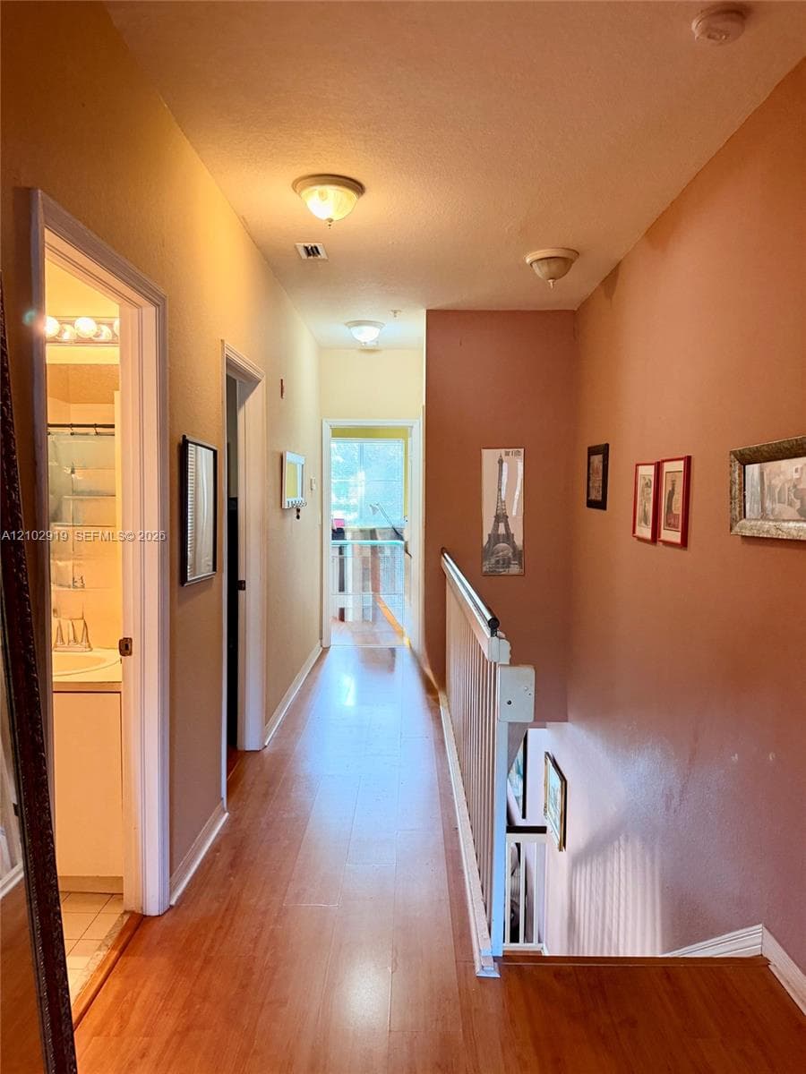 Hallway featuring wood-finish flooring, flush-mount ceiling lighting, and a painted railing with vertical balusters