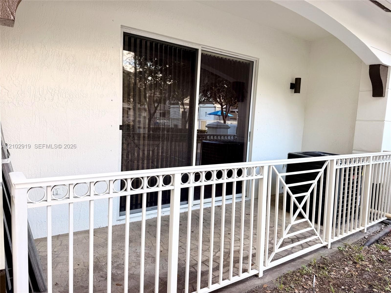 Covered patio featuring concrete pavers, white metal decorative railing, and sliding glass door