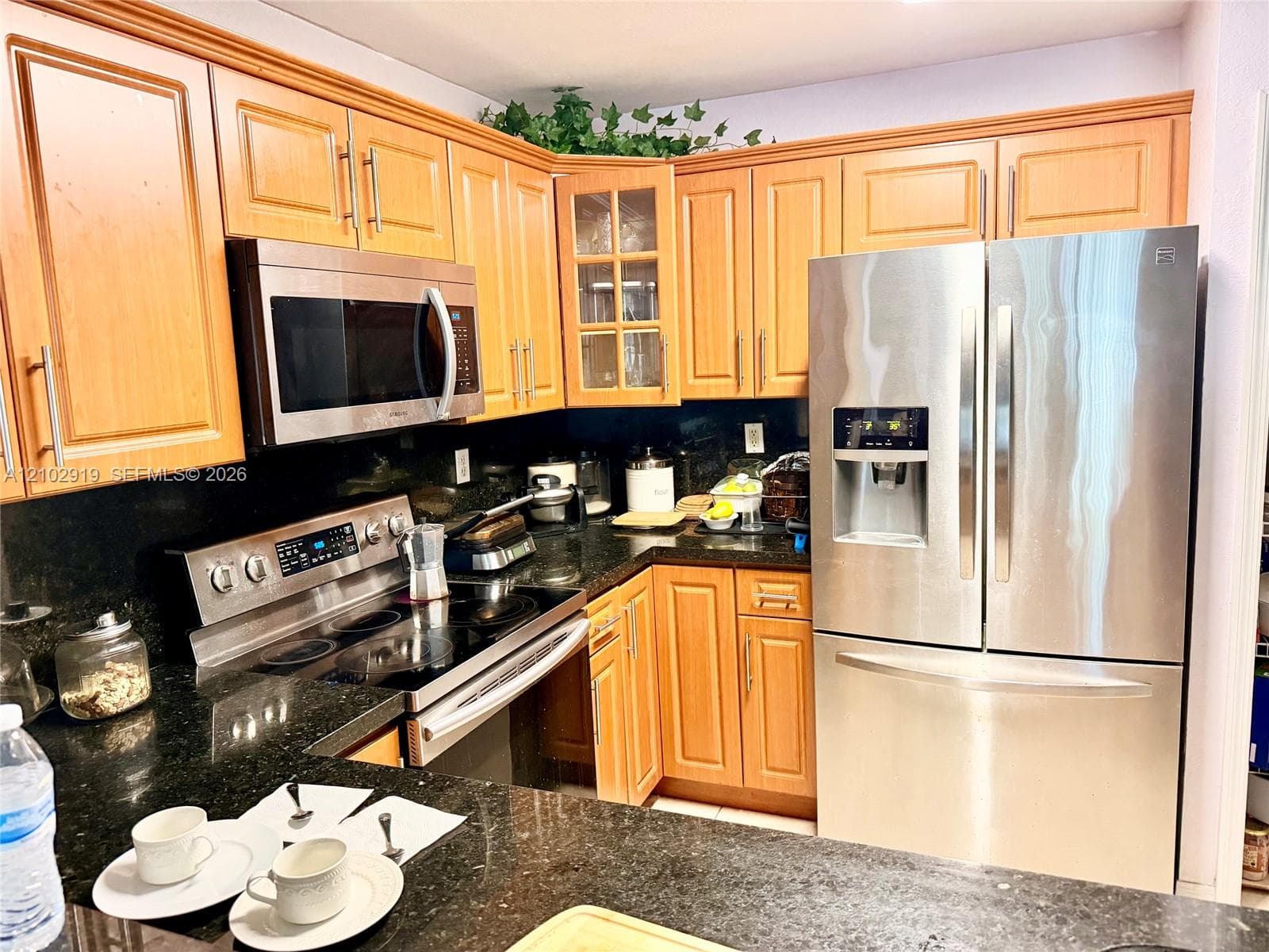 Kitchen featuring wood cabinetry, stainless steel appliances, dark stone countertops, and glass-front upper cabinet doors