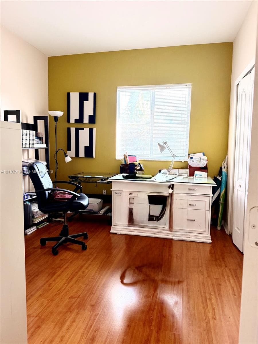 Room with wood-finish flooring, a central window with horizontal blinds, and a paneled closet door