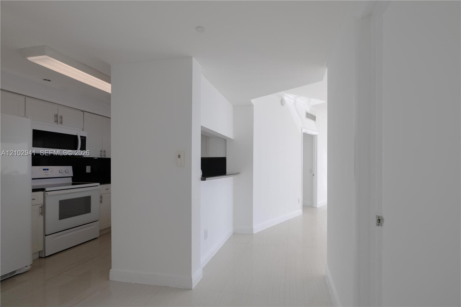 Kitchen featuring flat-panel white cabinetry, a black backsplash, integrated microwave, and a pass-through opening with a ledge