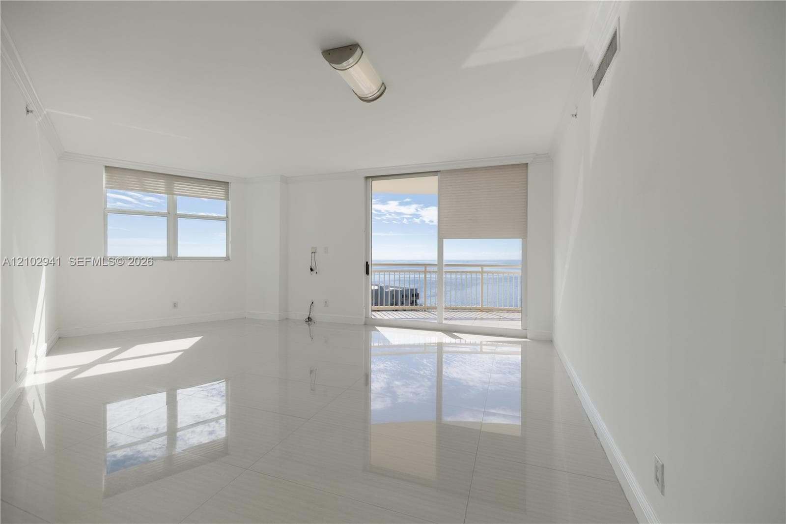 Bright living area featuring large-format polished tile flooring, sliding glass doors to a balcony, neutral wall tones, and expansive windows