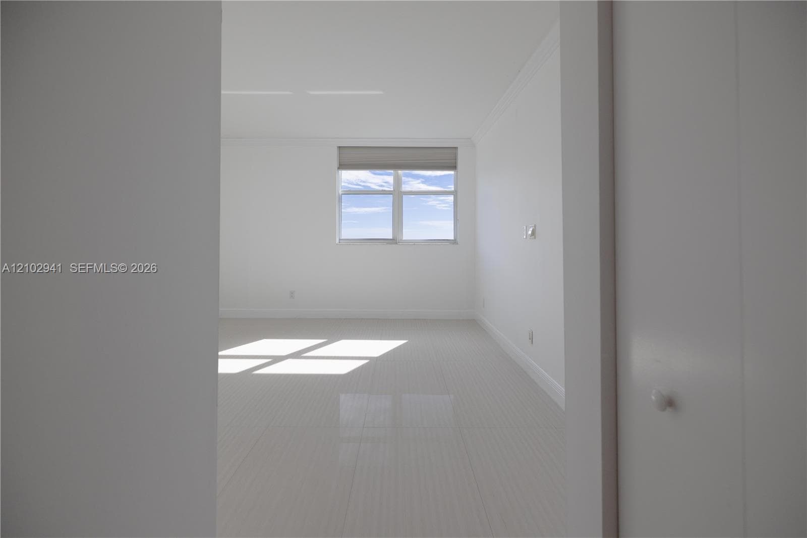 Neutral interior featuring large-format polished tile flooring, crisp white walls, crown molding, and a dual-pane window