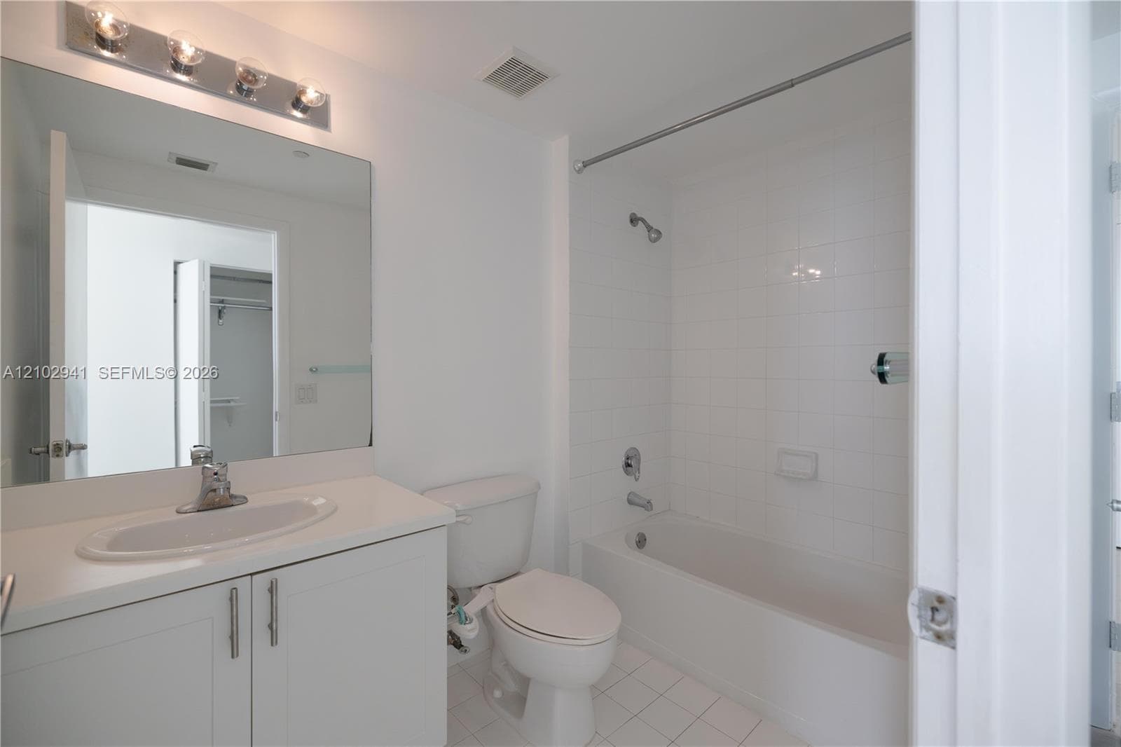 Bathroom featuring a vanity with an integrated oval sink, countertop, oversized wall mirror, four-light vanity fixture, and a tub-shower combination with white wall tile