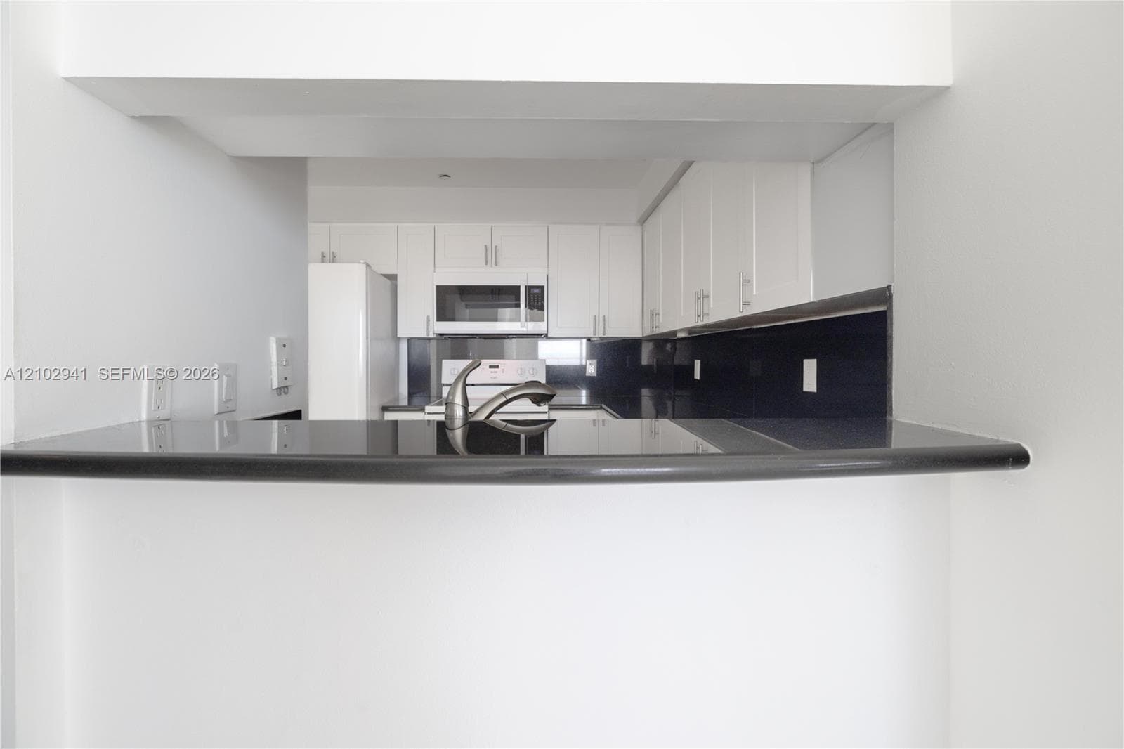 Kitchen featuring white cabinetry, contrasting dark countertops, a dark backsplash, a built-in microwave, and a stainless steel faucet