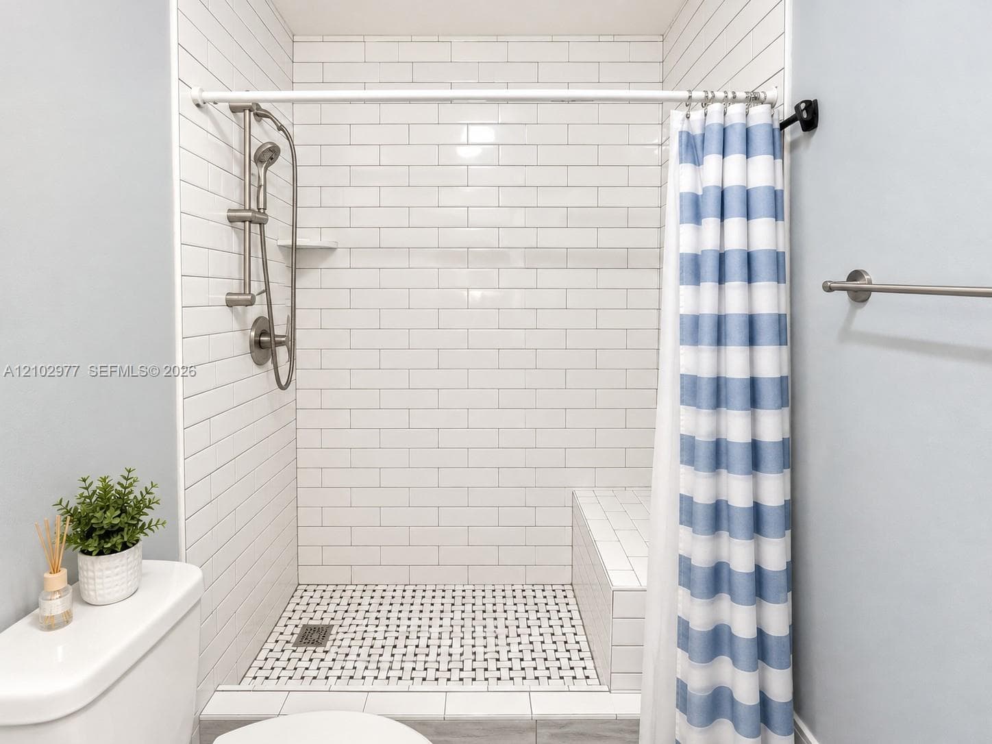 Walk-in shower featuring white subway tile surround, integrated tiled bench, basketweave tile floor, and adjustable-height handheld shower fixture