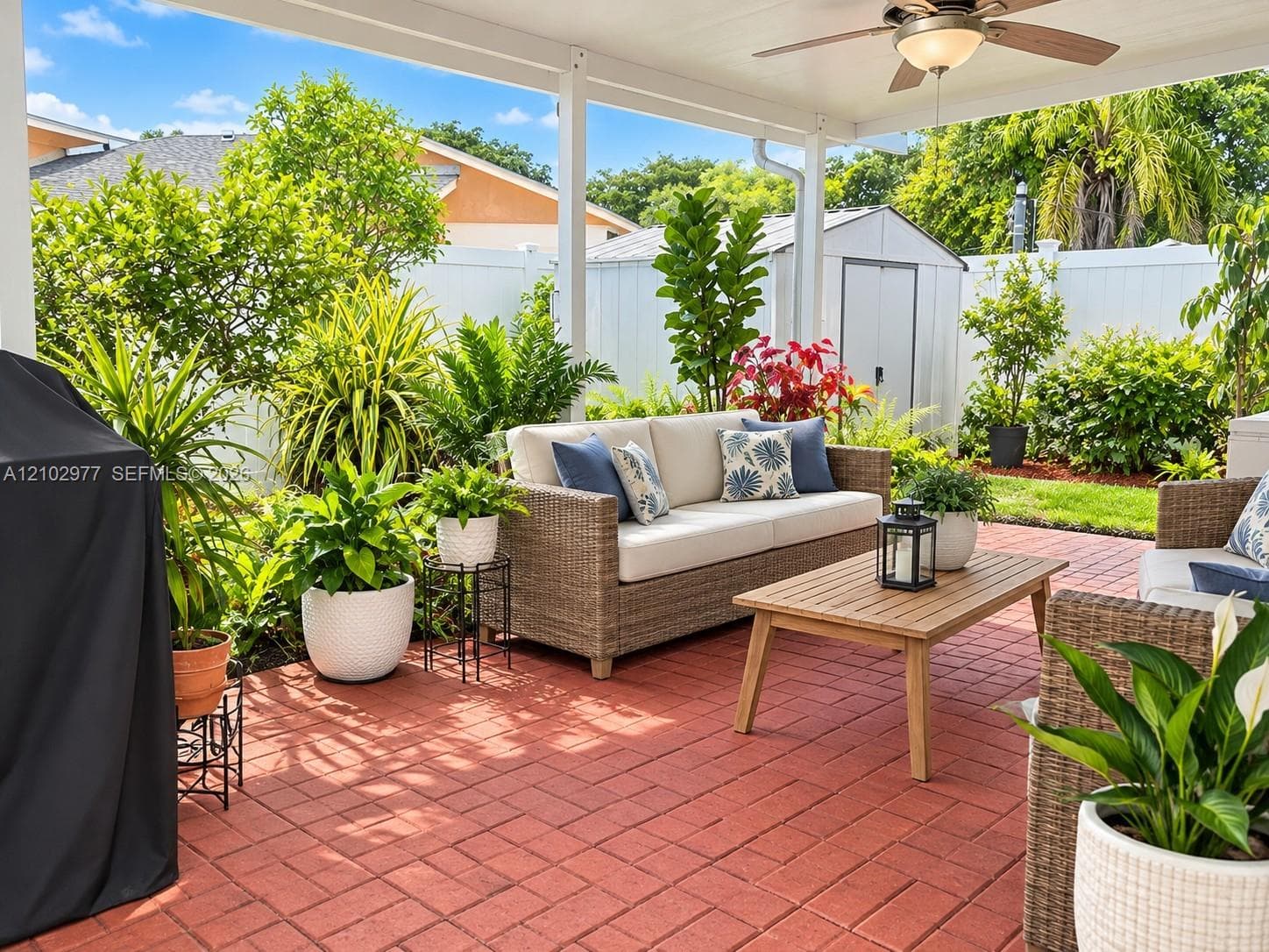 Covered patio featuring red brick pavers, ceiling-mounted paddle fan with integrated light, and solid white vinyl perimeter fencing