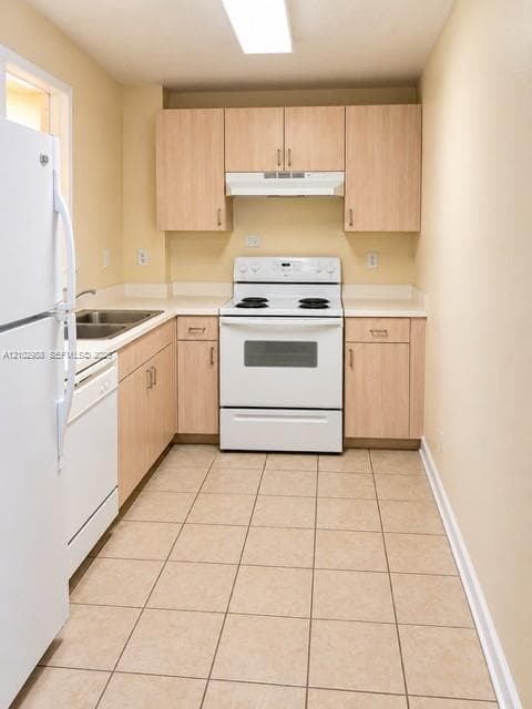 Kitchen featuring light wood-finish cabinetry, tile flooring, white appliances, and a double-basin sink with solid-surface countertops