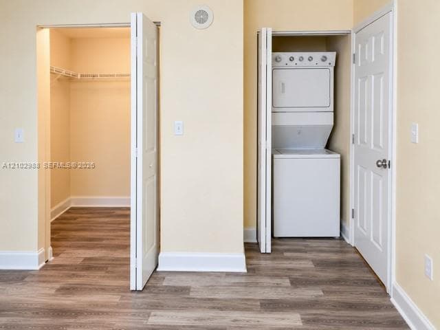 Walk-in closet with built-in wire shelving, stacked laundry unit, wood-finish flooring, and six-panel interior doors