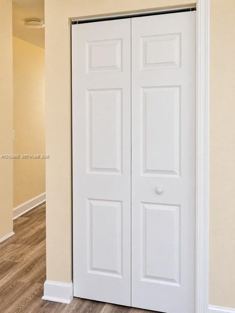 White six-panel bi-fold closet doors featuring a central knob, paired with wood-finish flooring