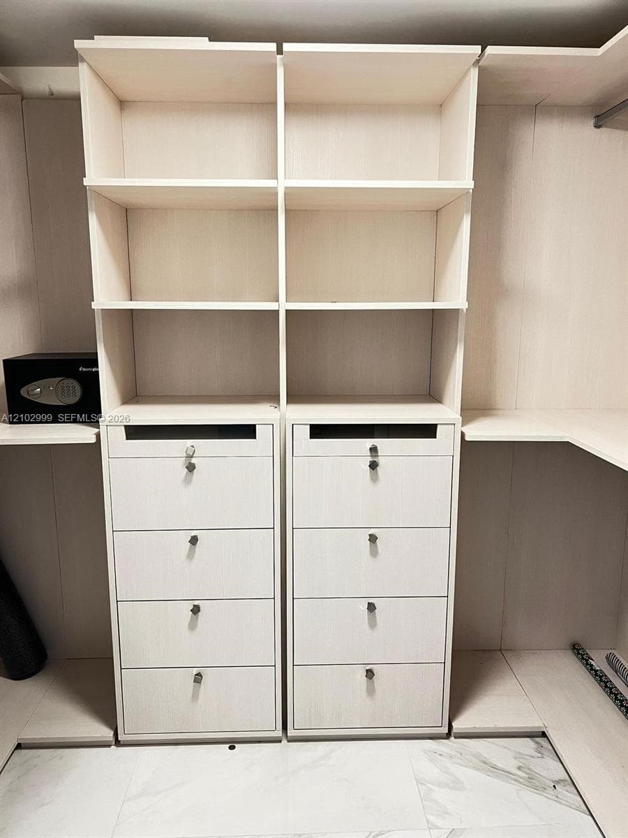 Custom closet organization featuring light-toned wood-finish cabinetry, built-in shelving, eight stackable drawers with locking mechanisms, and integrated hanging rods
