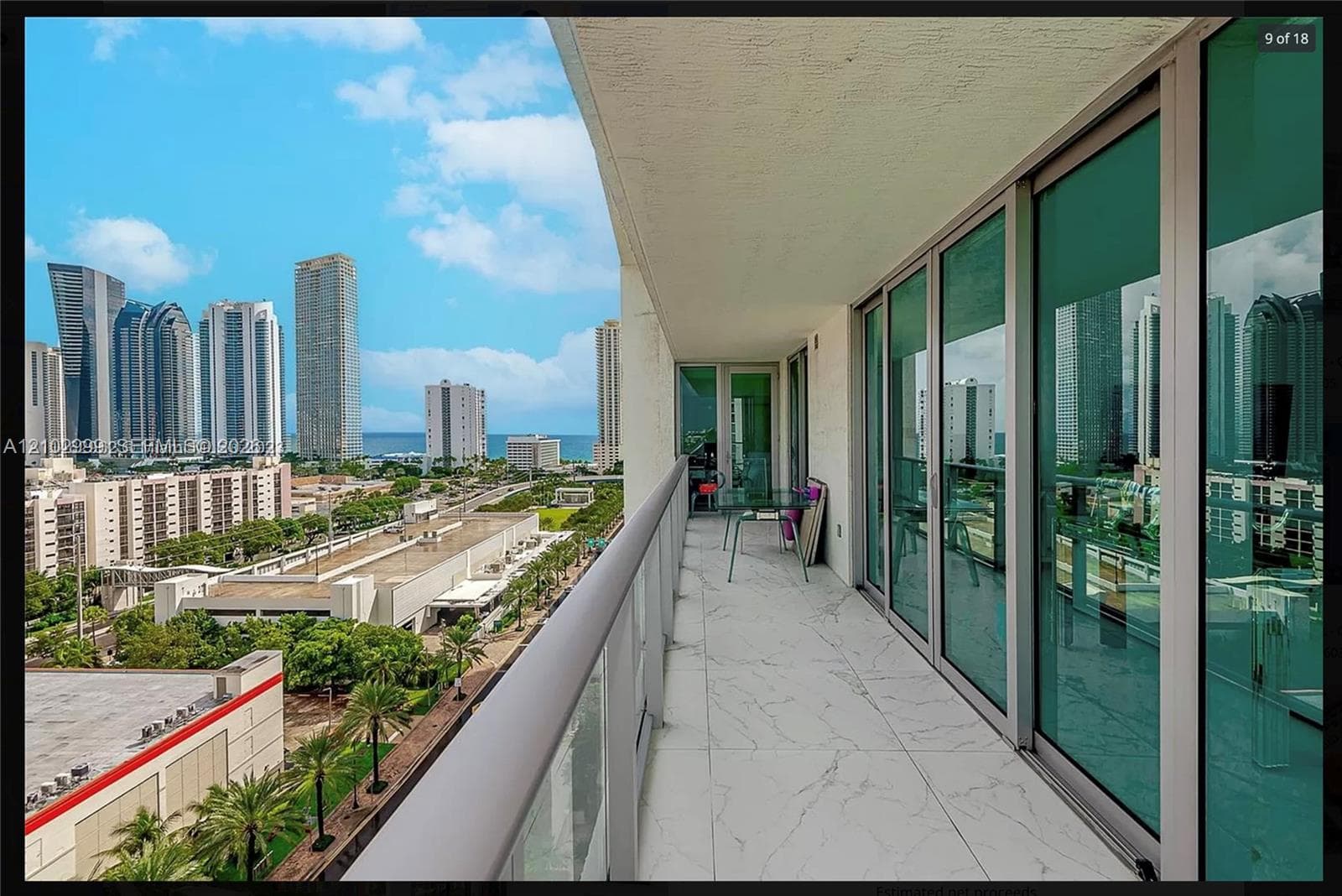Balcony with a glass and metal railing, large format light-toned tile flooring, and multiple full-height sliding glass doors