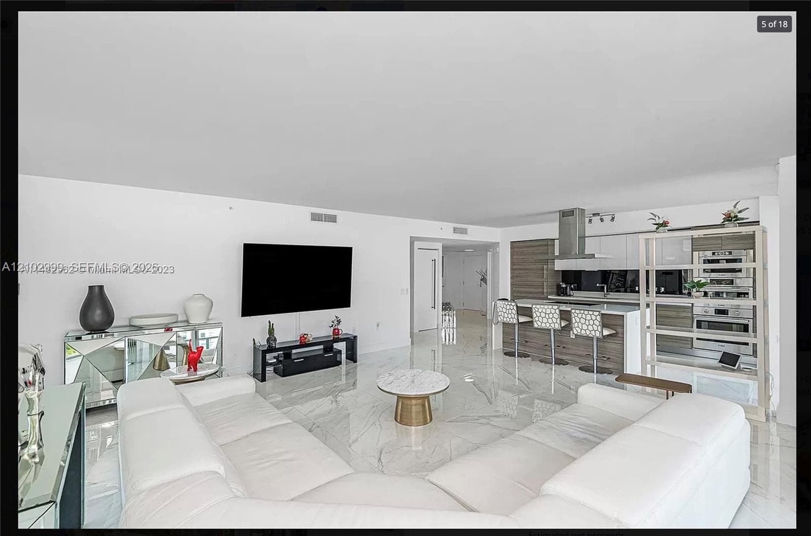 Open-concept living space featuring high ceilings, large-format polished tile flooring, a contemporary kitchen island with seating, stainless steel range hood, and integrated stainless steel appliances