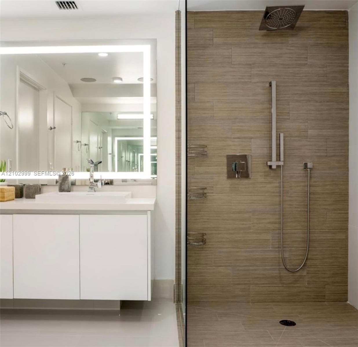 Floating vanity with integrated sink, backlit vanity mirror, glass-enclosed shower, rain shower head, and tiled shower walls