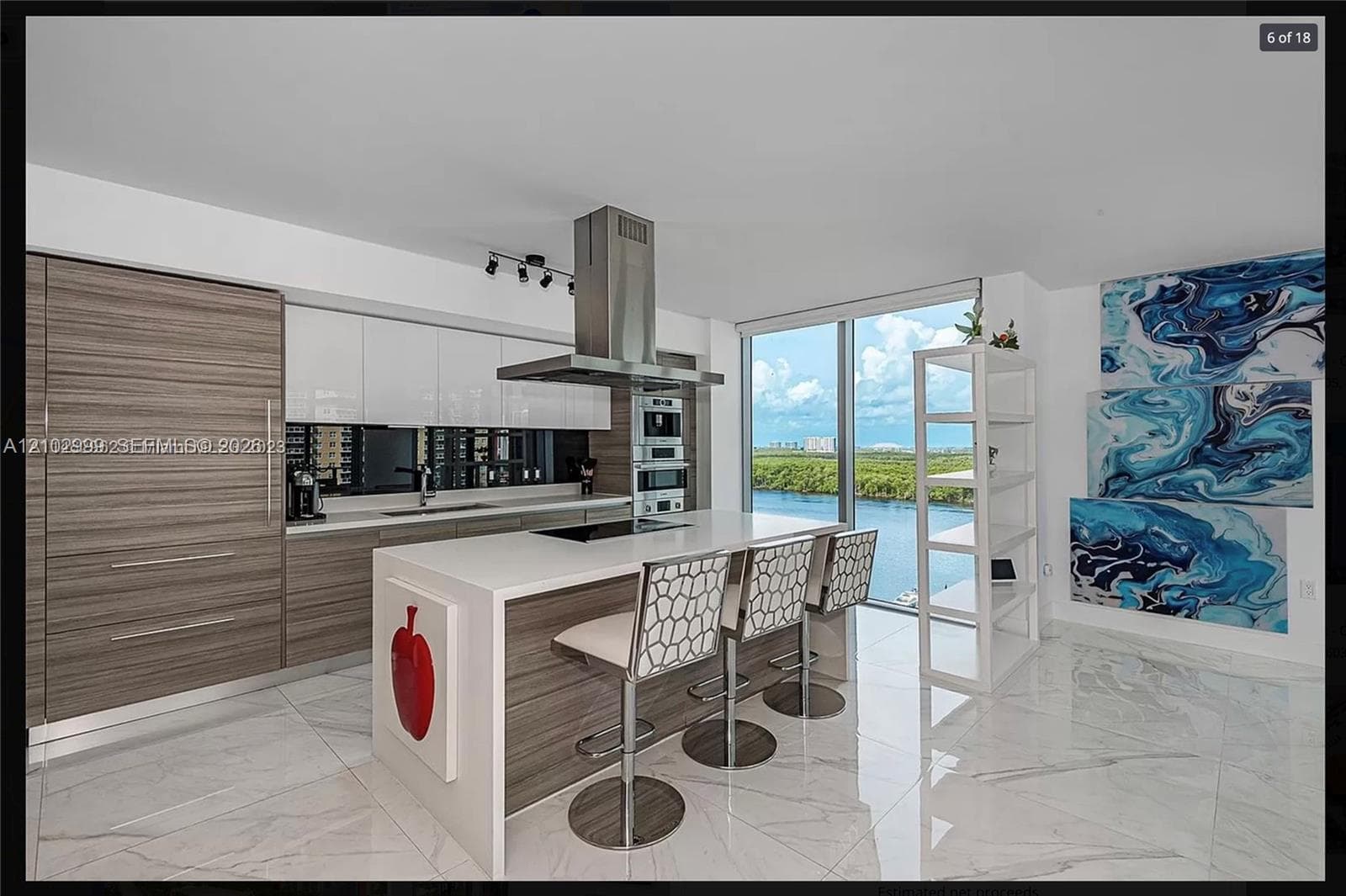 Modern kitchen featuring an expansive island with seating, a stainless steel range hood, integrated appliances, and floor-to-ceiling windows with a prominent water backdrop