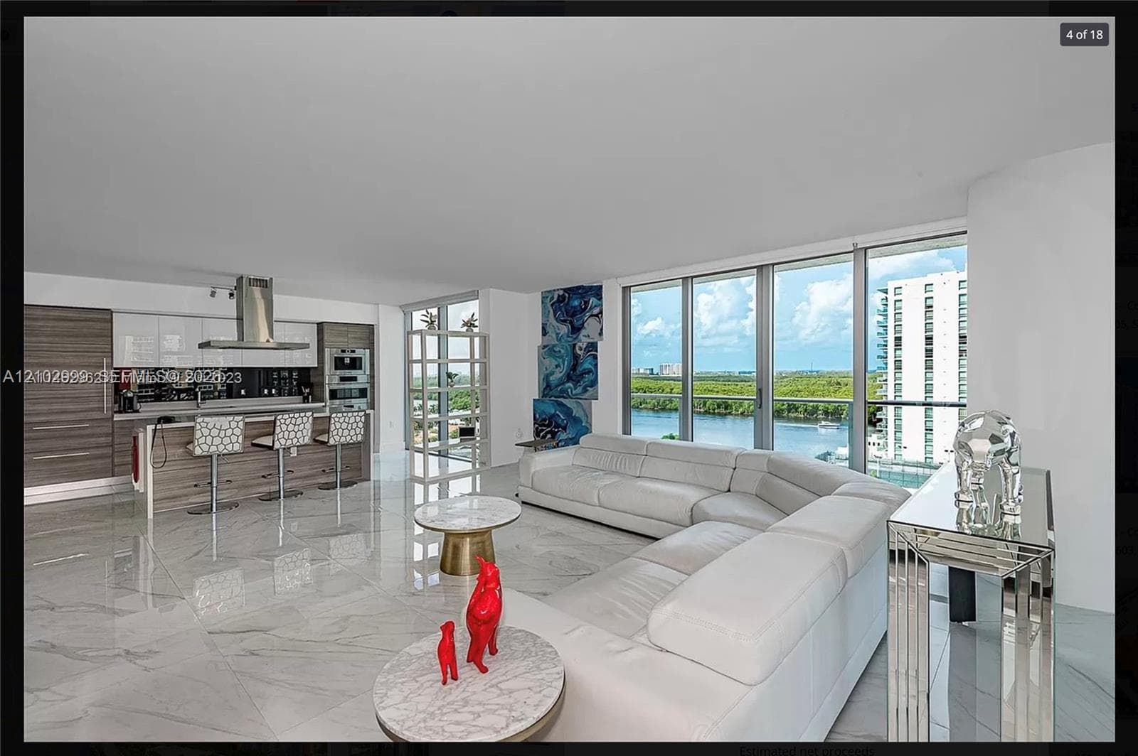 Open-concept living area with large format tile flooring, a modern kitchen island with seating, stainless steel appliances, and floor-to-ceiling windows
