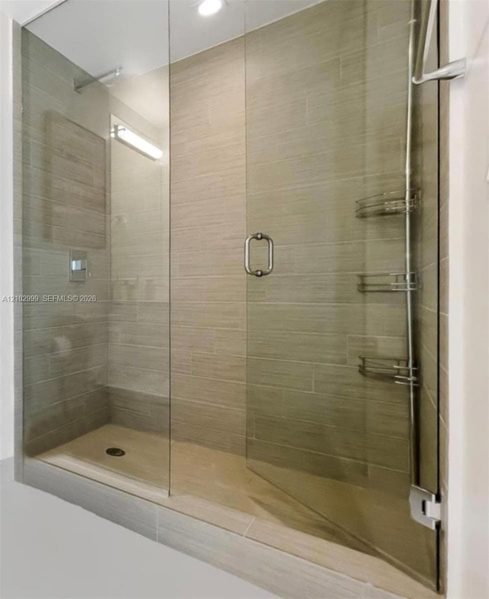 Glass-enclosed shower featuring large format wall tiles, a built-in shower bench, and a tiled shower pan