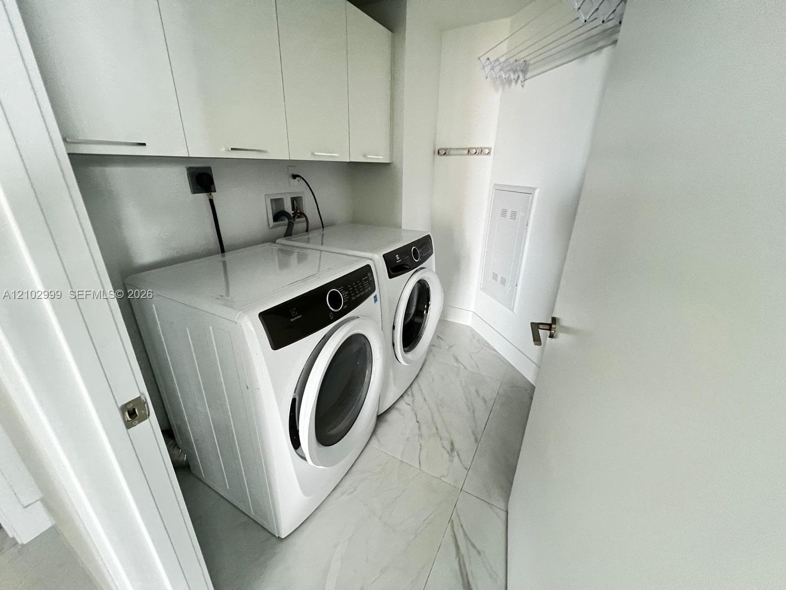 Laundry area featuring white flat-panel upper cabinetry, large-format tile flooring, and a wall-mounted drying rack