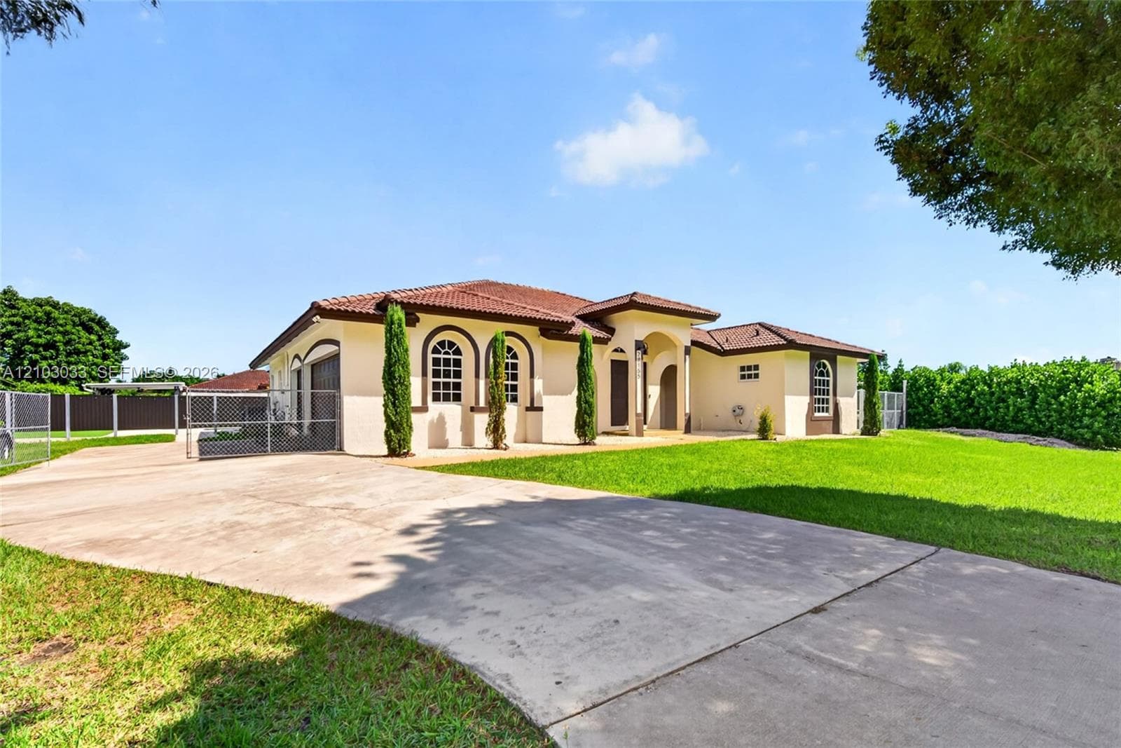 Single-story stucco exterior featuring a tile roof, arched windows, covered entryway, and a concrete driveway