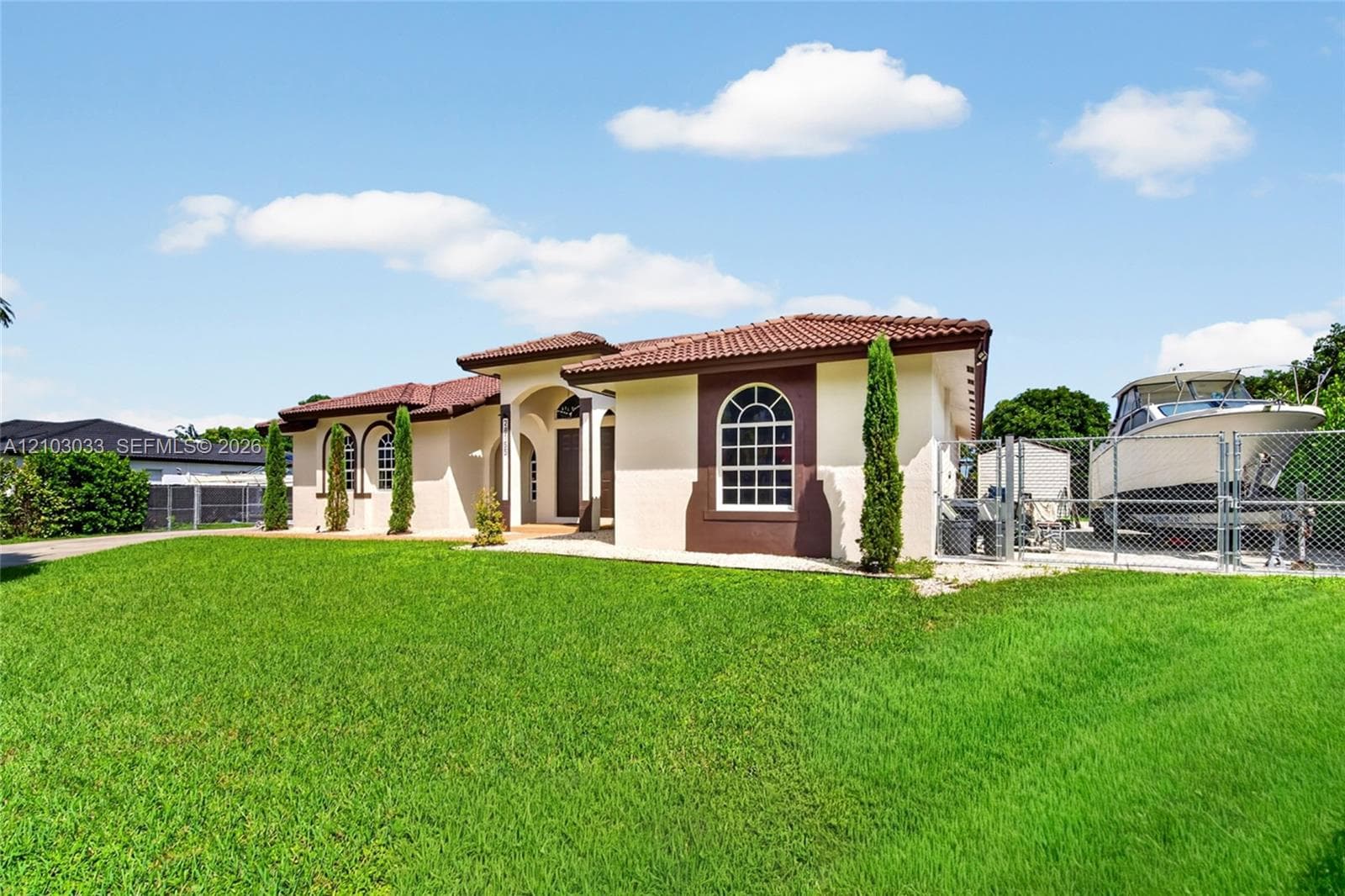 Stucco exterior featuring arched windows, a multi-hip clay tile roof, covered entryway, and gated side yard storage