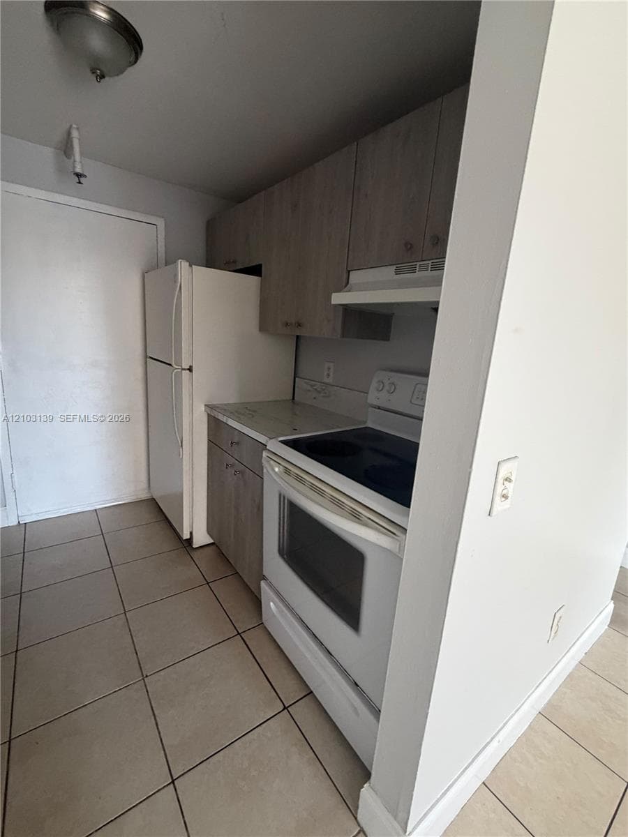 Kitchen featuring tile flooring, wood-finish cabinetry, and white appliances including a refrigerator and range