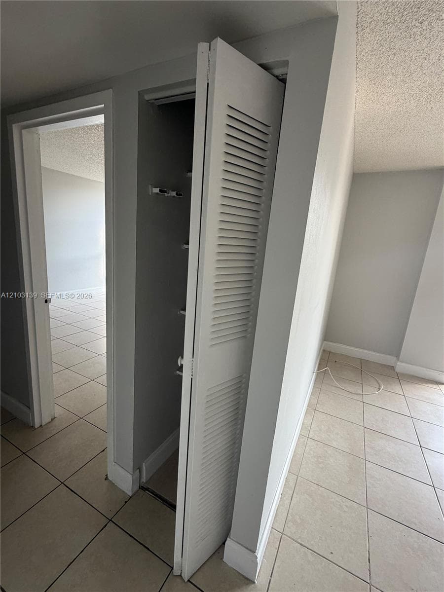 Louvered bi-fold doors enclosing a storage area, with tile flooring extending into the adjacent room