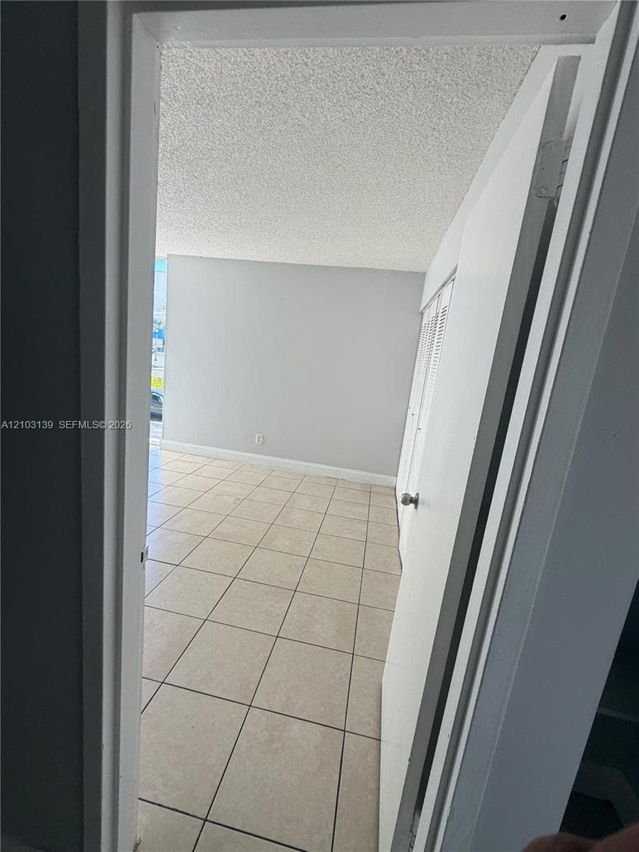 Light-colored square tile flooring, neutral wall color, and a textured ceiling