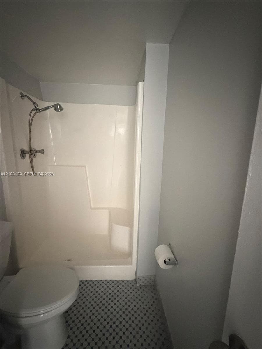Shower with chrome fixtures and integrated seating, white toilet, and patterned tile flooring
