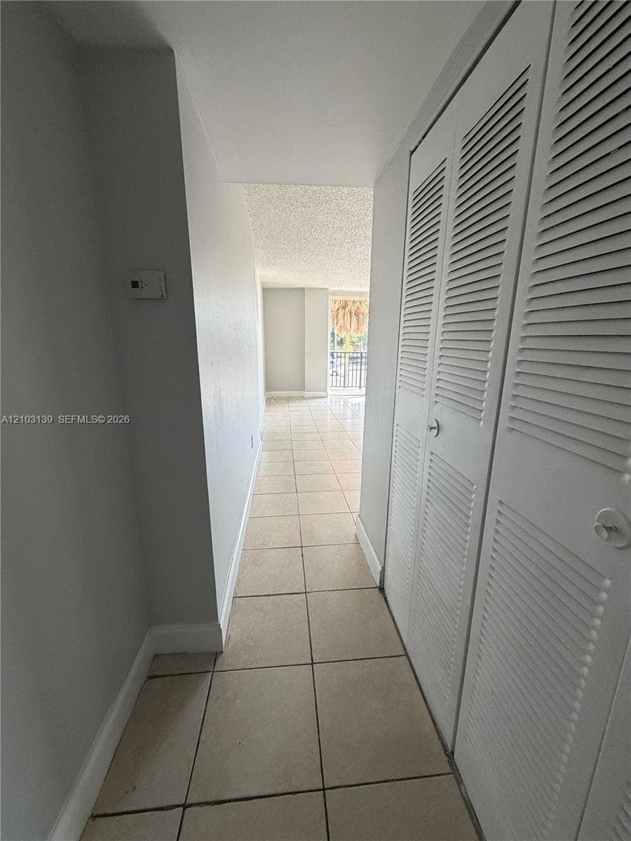 Recessed hallway with tile flooring, louvered bi-fold closet doors, and light-toned walls