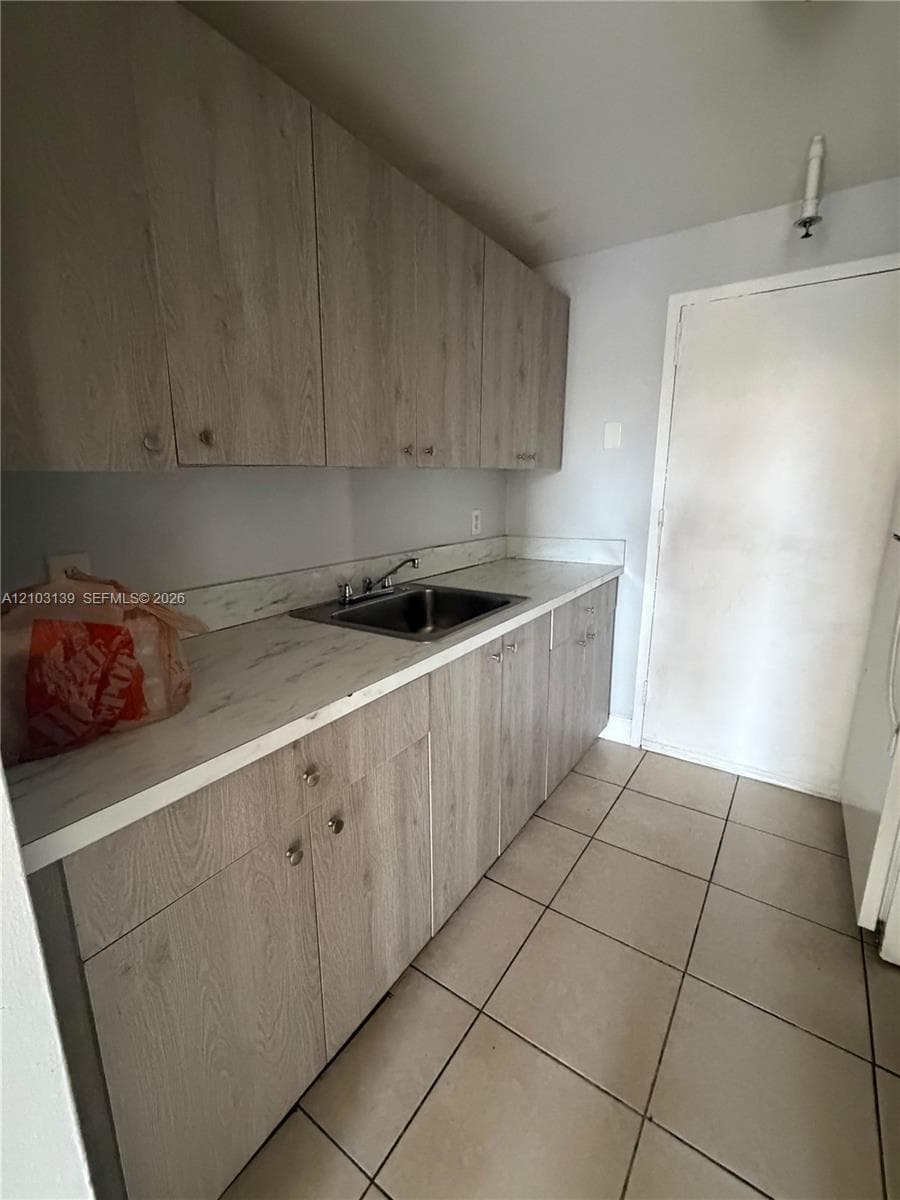Wood-finish cabinetry with silver hardware, laminate countertops, stainless steel sink, and large format floor tiling