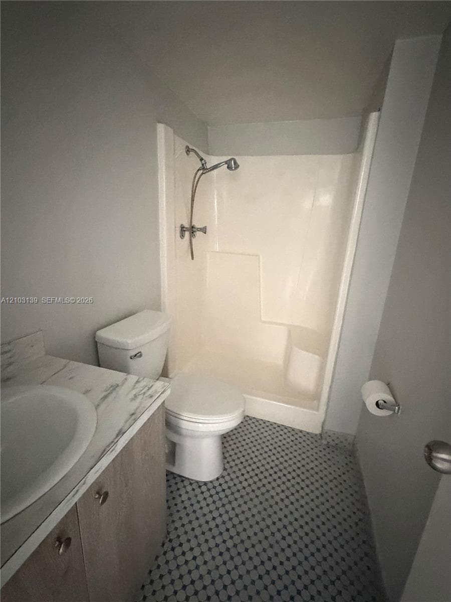 Bathroom with a shower enclosure, toilet, and vanity featuring an integrated sink, wood-finish cabinetry, and a light-toned countertop