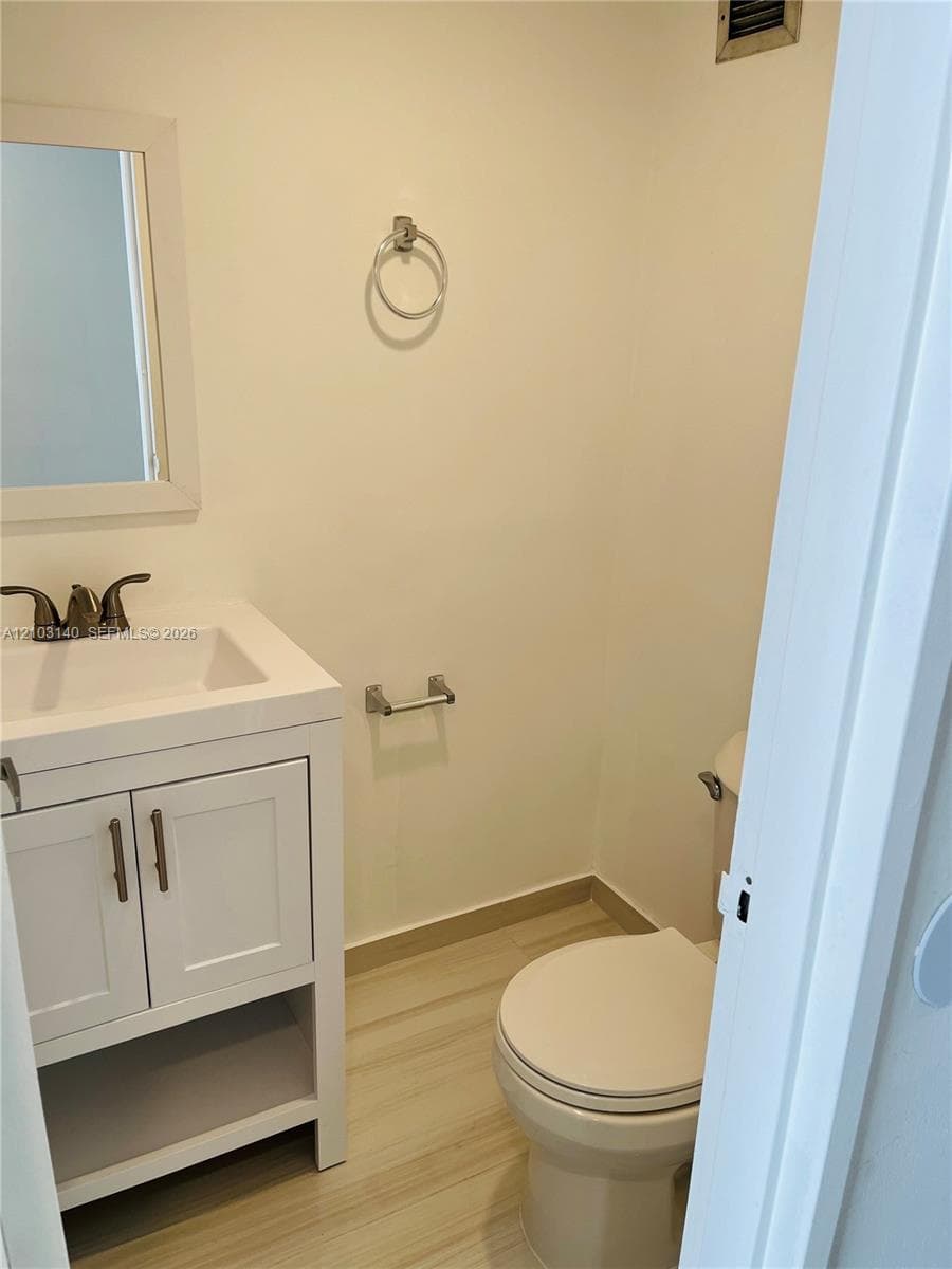 White vanity with shaker-style cabinet doors, integrated sink, bronze-tone faucet, framed wall mirror, and neutral wood-finish flooring