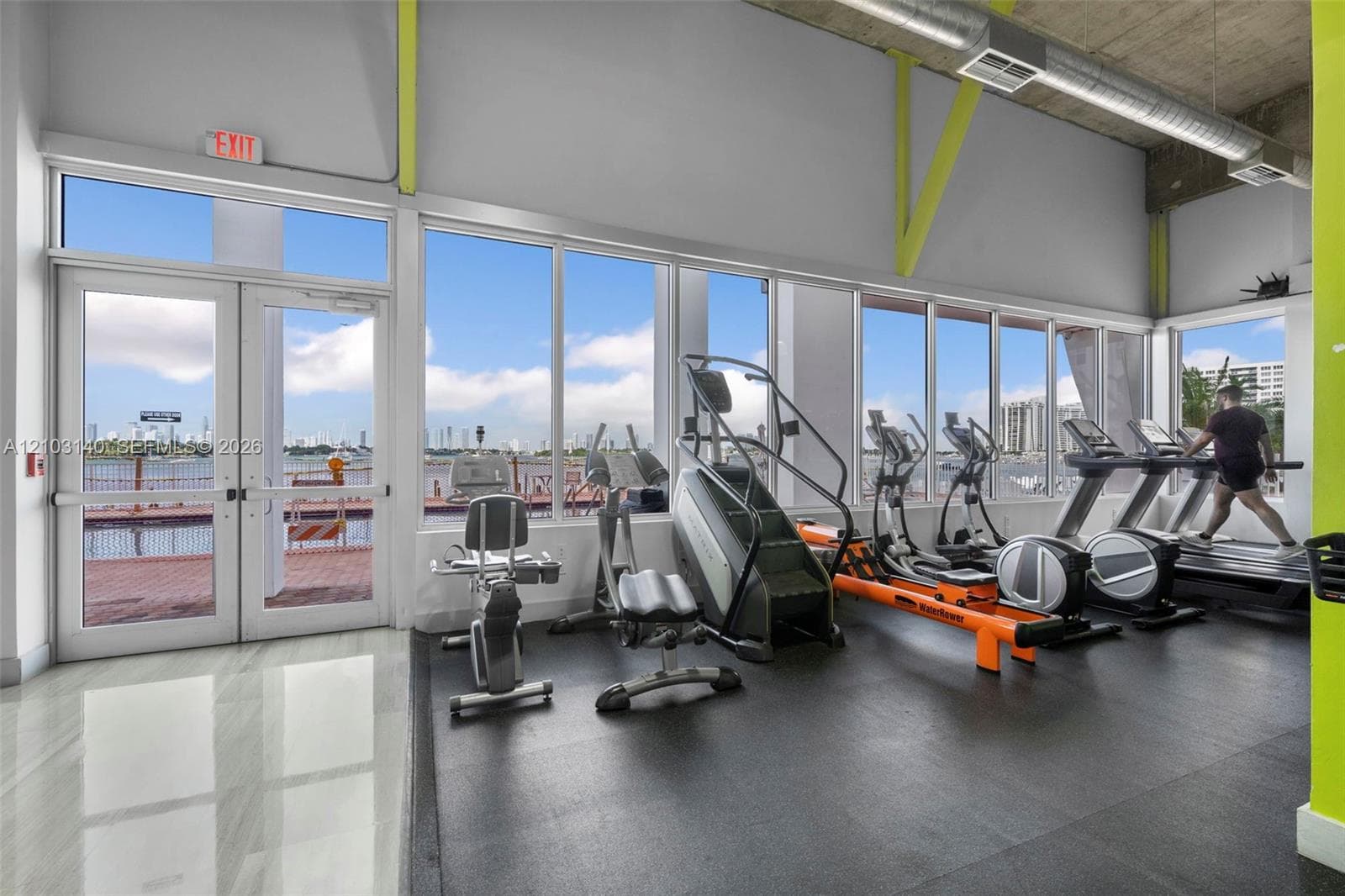 Fitness area featuring floor-to-ceiling windows, exposed industrial ceiling with ductwork, rubberized flooring, and double-glass door exterior access
