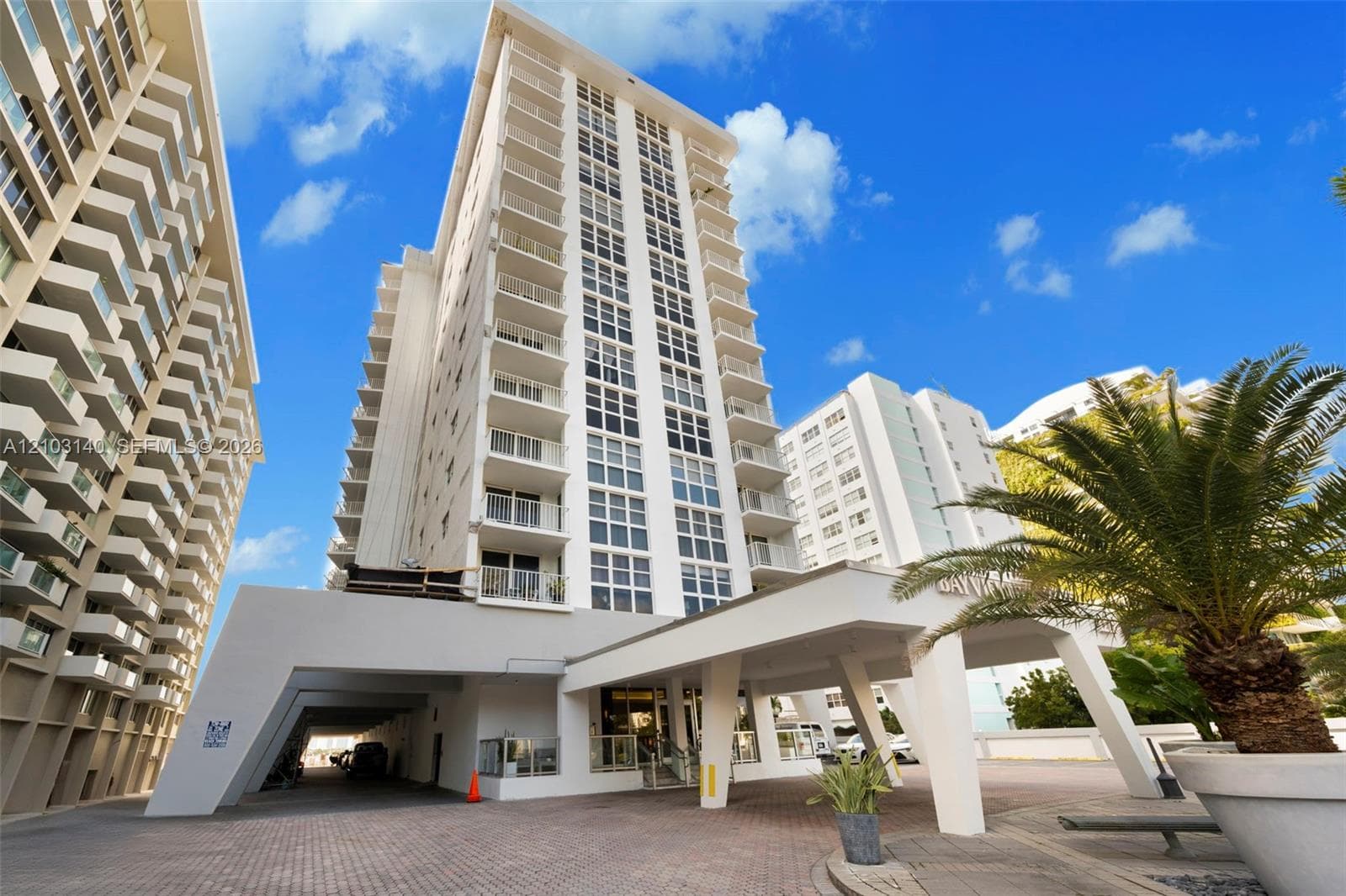 High-rise building exterior featuring a covered porte-cochère, multi-level balconies, masonry paver driveway, and structural angular design